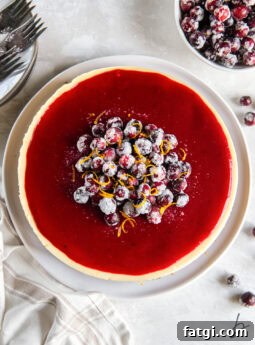 tabletop with cranberry cheesecake topped with glossy cranberry glaze and sugar cranberries.