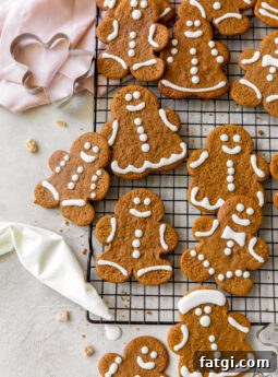 iced gingerbread man cookies on wire cooling rack next to pink kitchen cloth and icing bag with royal icing