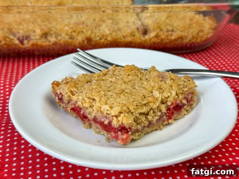 Beautiful cherry fruit bar with a golden brown baked oatmeal top and bottom on a small plate with the glass baking dish on a red napkin with white dots.
