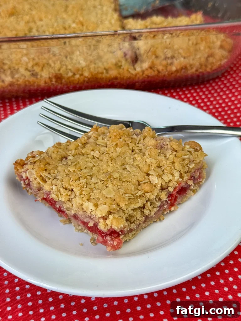 Earthly oatmeal sweetened with brown sugar baked with a layer of cherry pie filling in the center and served on a white plate with a fork and the full baking pan in the background.