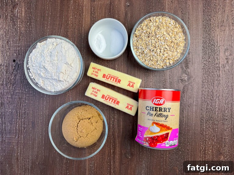 Ingredients to make Oatmeal Fruit Bars are flour, baking soda, salt, quick oats, butter, brown sugar and a can of cherry pie filling on a wooden counter top.