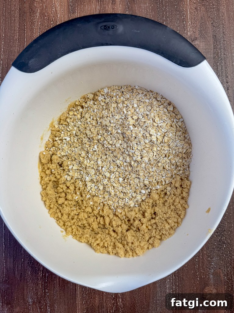 Quick oats poured on top of a brown sugar and butter crumb mixture in a white bowl.