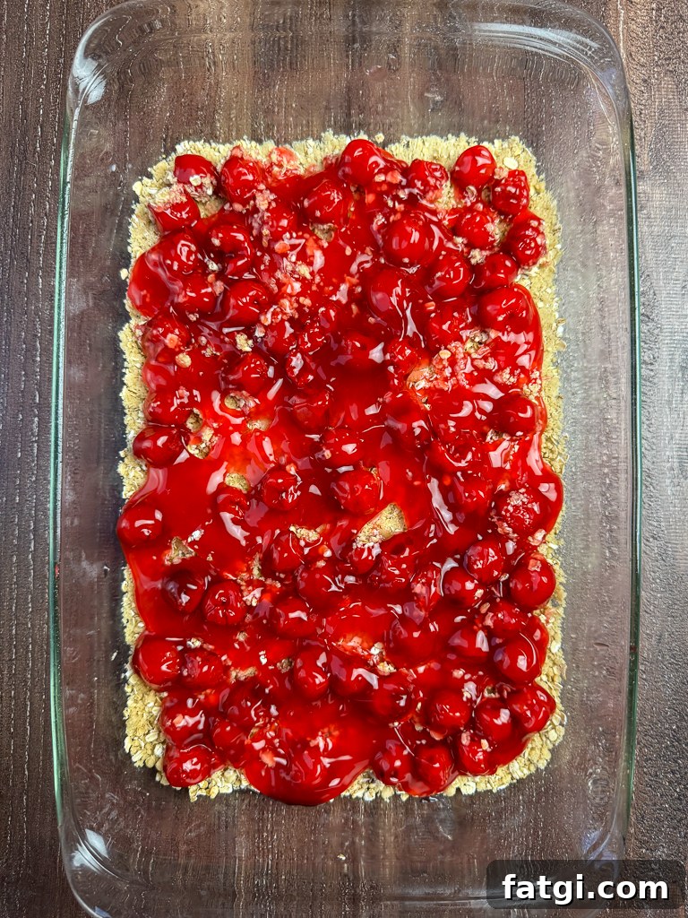 Can of cherry pie filling spooned over top of base layer to make an oatmeal fruit bars recipe.