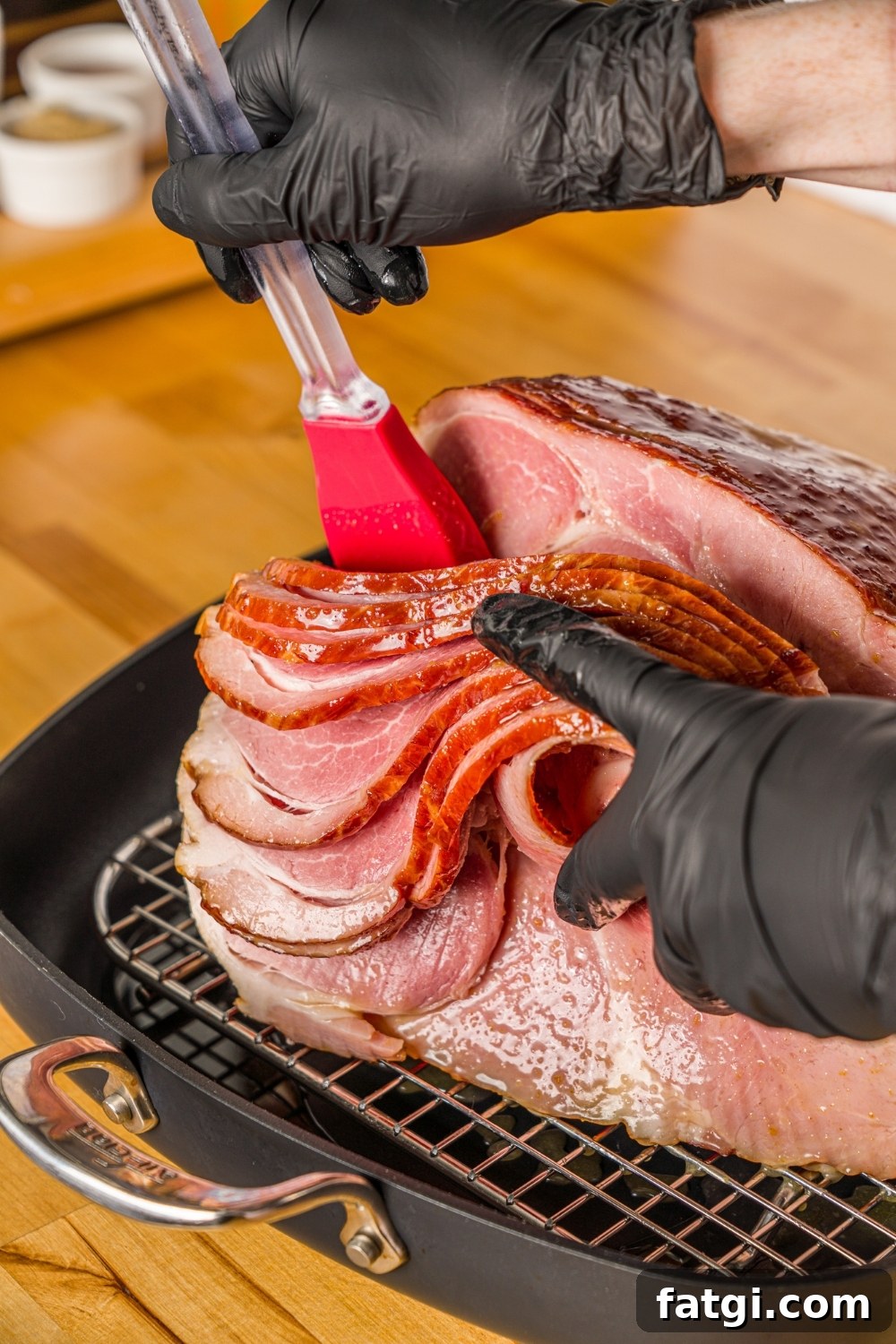 Spiral Ham with Pineapple and Brown Sugar Glaze 6 An uncooked spiral ham on a roasting pan lined with a rack. There is a hand brushing glaze inside the slices of the ham.
