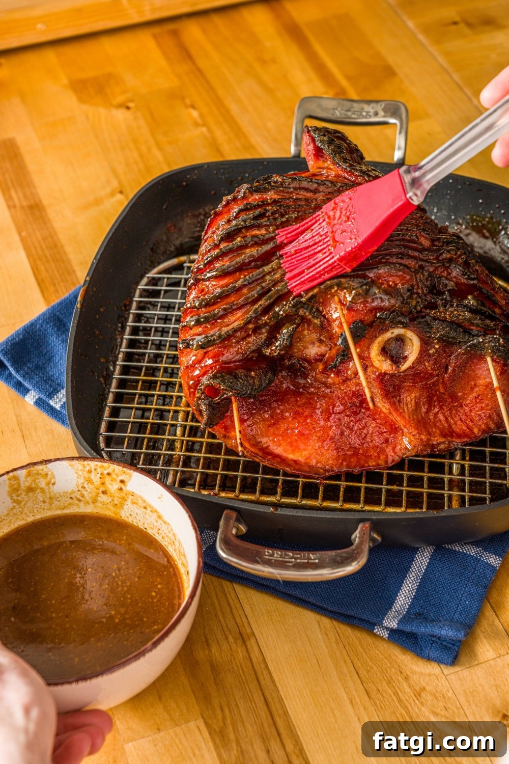 Spiral Ham with Pineapple and Brown Sugar Glaze 9 A glazed spiral ham on a roasting pan lined with a rack. The ham is being brushed with glaze.