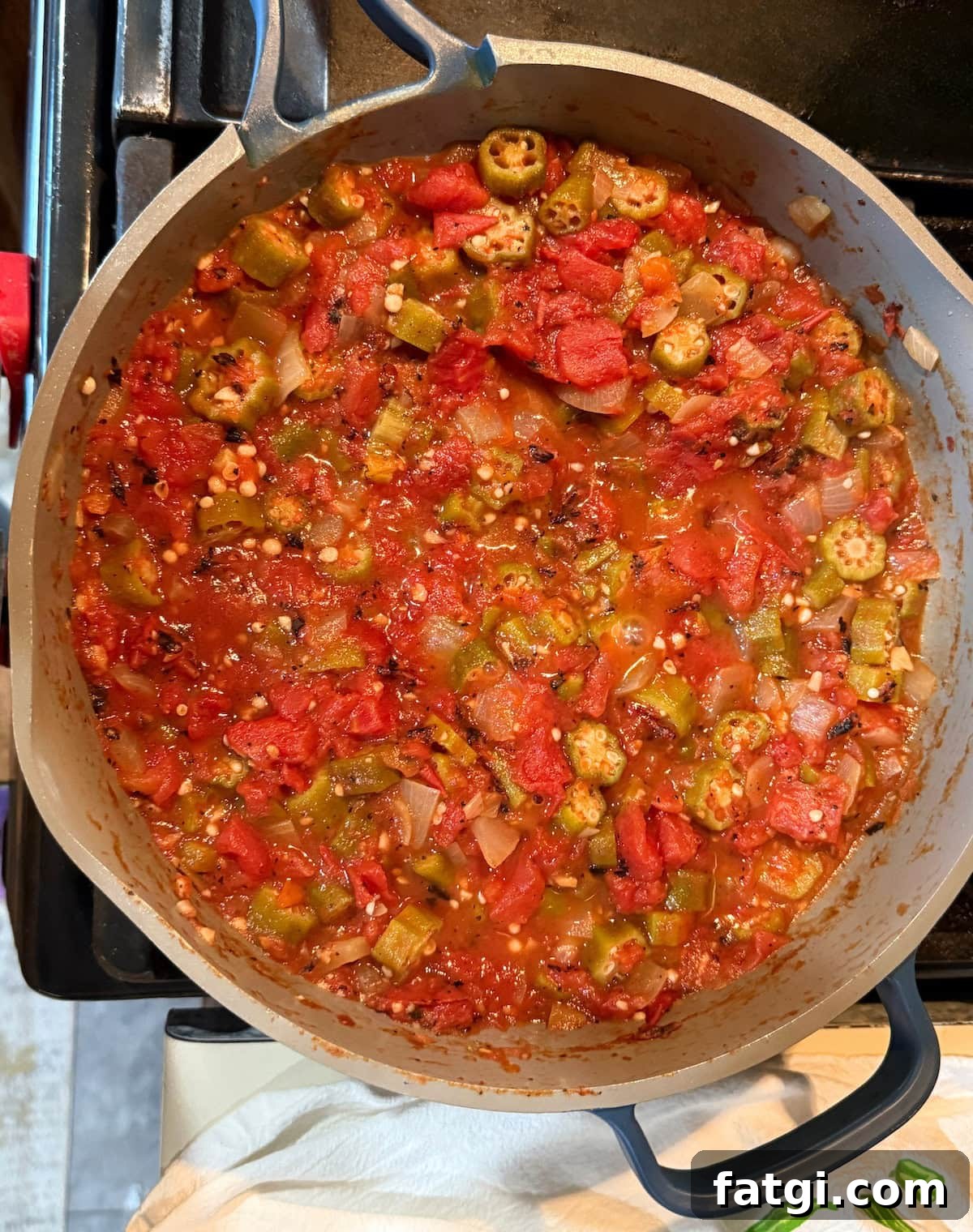 A pot filled with a colorful stew made from diced tomatoes, okra, green peppers, and onions, simmering on a stovetop.