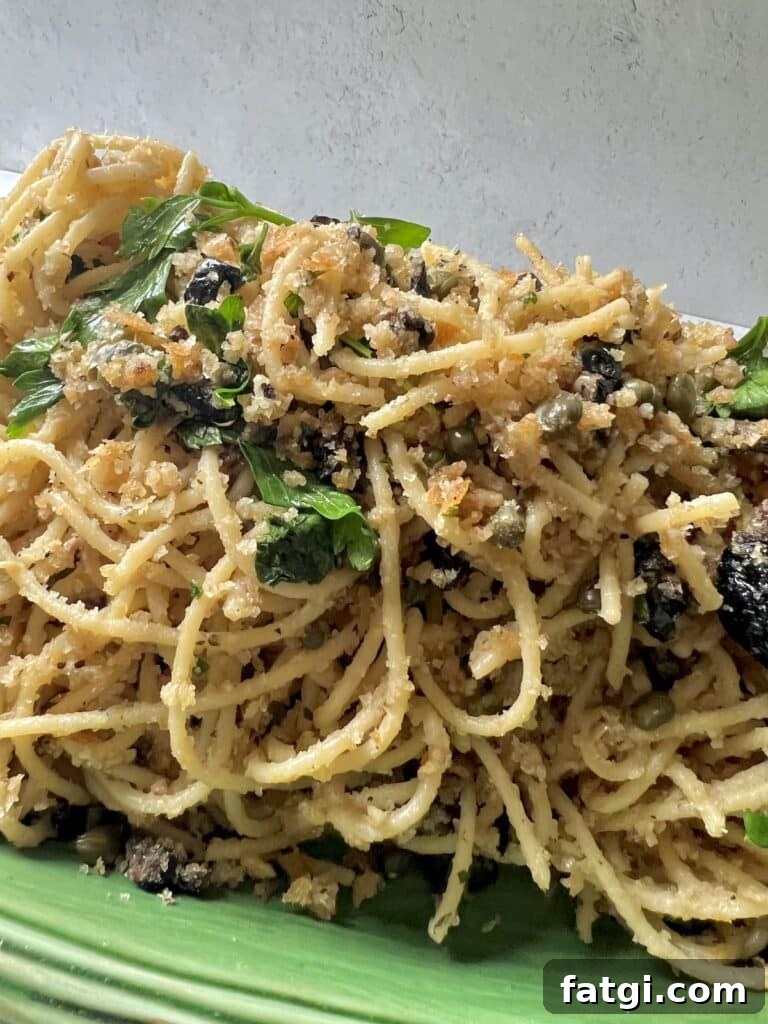 Spaghetti with Breadcrumbs and Anchovies on green platter with parsley garnish.