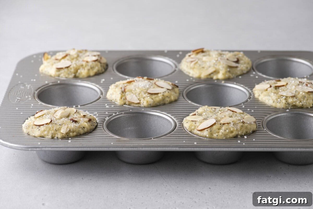 Almond Poppy Seed Muffins Recipe 11 A metal muffin tin holds unbaked muffins topped with sliced almonds and coarse sugar.