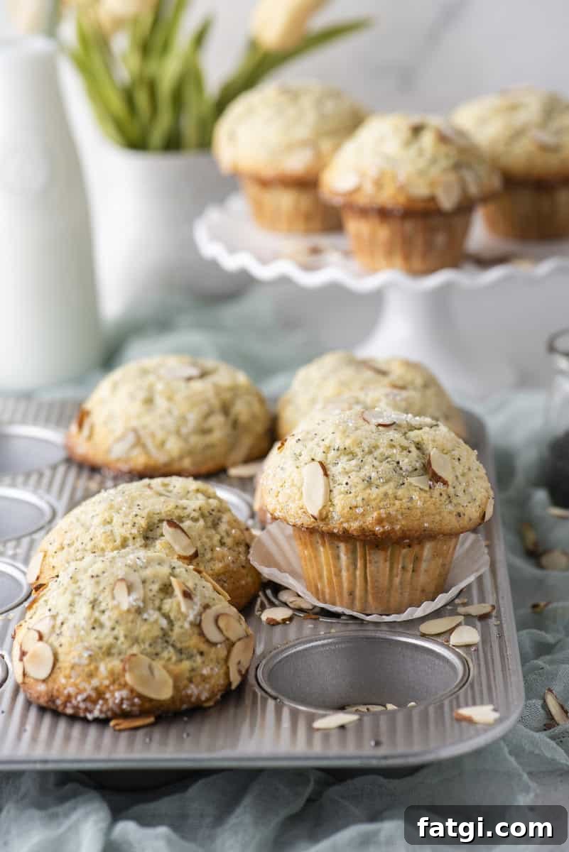 Almond Poppy Seed Muffins Recipe 13 A close-up of freshly baked almond muffins in a muffin tin, with sliced almonds on top.