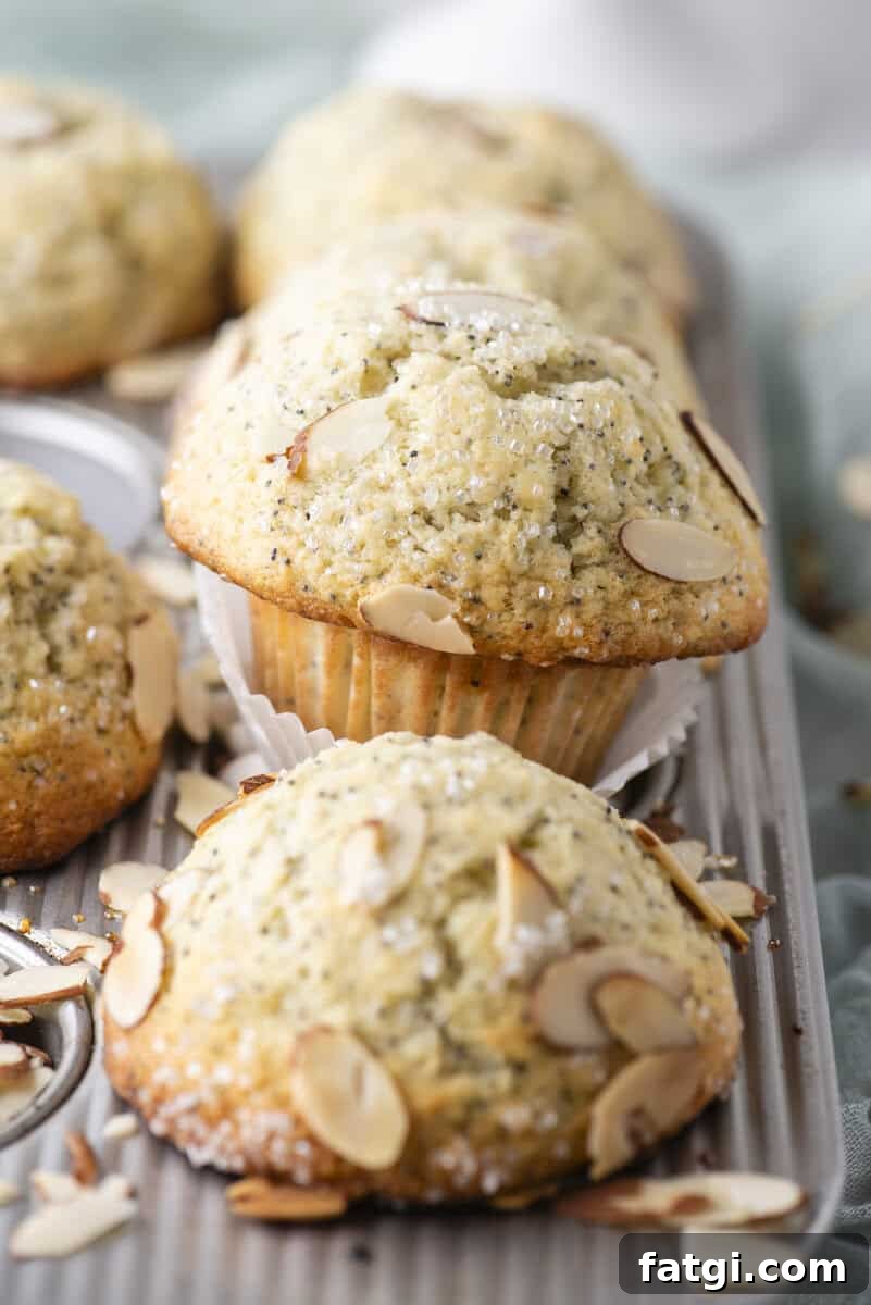 Almond Poppy Seed Muffins Recipe 14 Freshly baked almond poppy seed muffins in a metal muffin tray, topped with sliced almonds and sugar crystals.