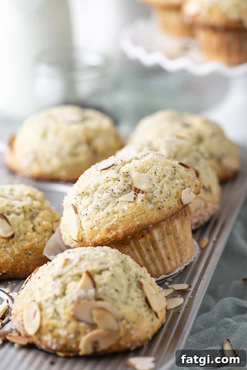 Almond Poppy Seed Muffins Recipe 15 Freshly baked almond poppy seed muffins are arranged on a metal cooling rack, topped with sliced almonds and coarse sugar.