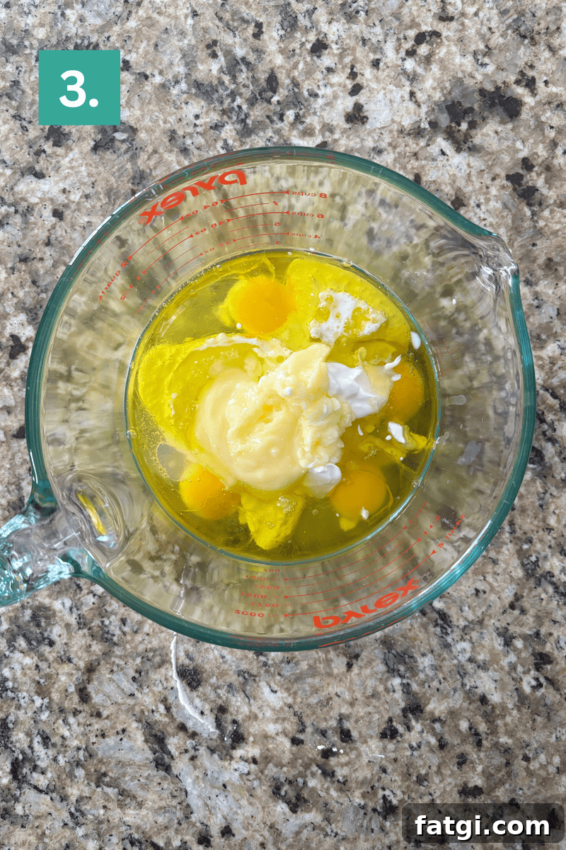 Almond Poppy Seed Muffins Recipe 7 A glass Pyrex measuring cup containing eggs and wet ingredients sitting on a granite countertop.