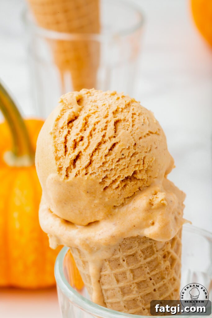 a sugar cone with a scoop of pumpkin spice ice cream, propped up in a glass. There is a pumpkin in the background.
