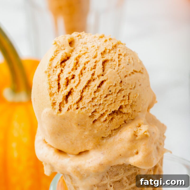 a sugar cone with a scoop of pumpkin spice ice cream, propped up in a glass. There is a pumpkin in the background.