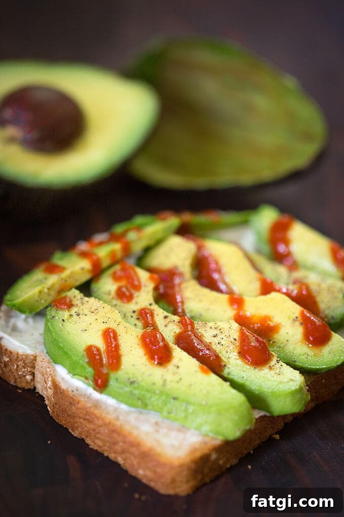 Sliced avocado on bread with drizzle of hot sauce with cut avocado in the background