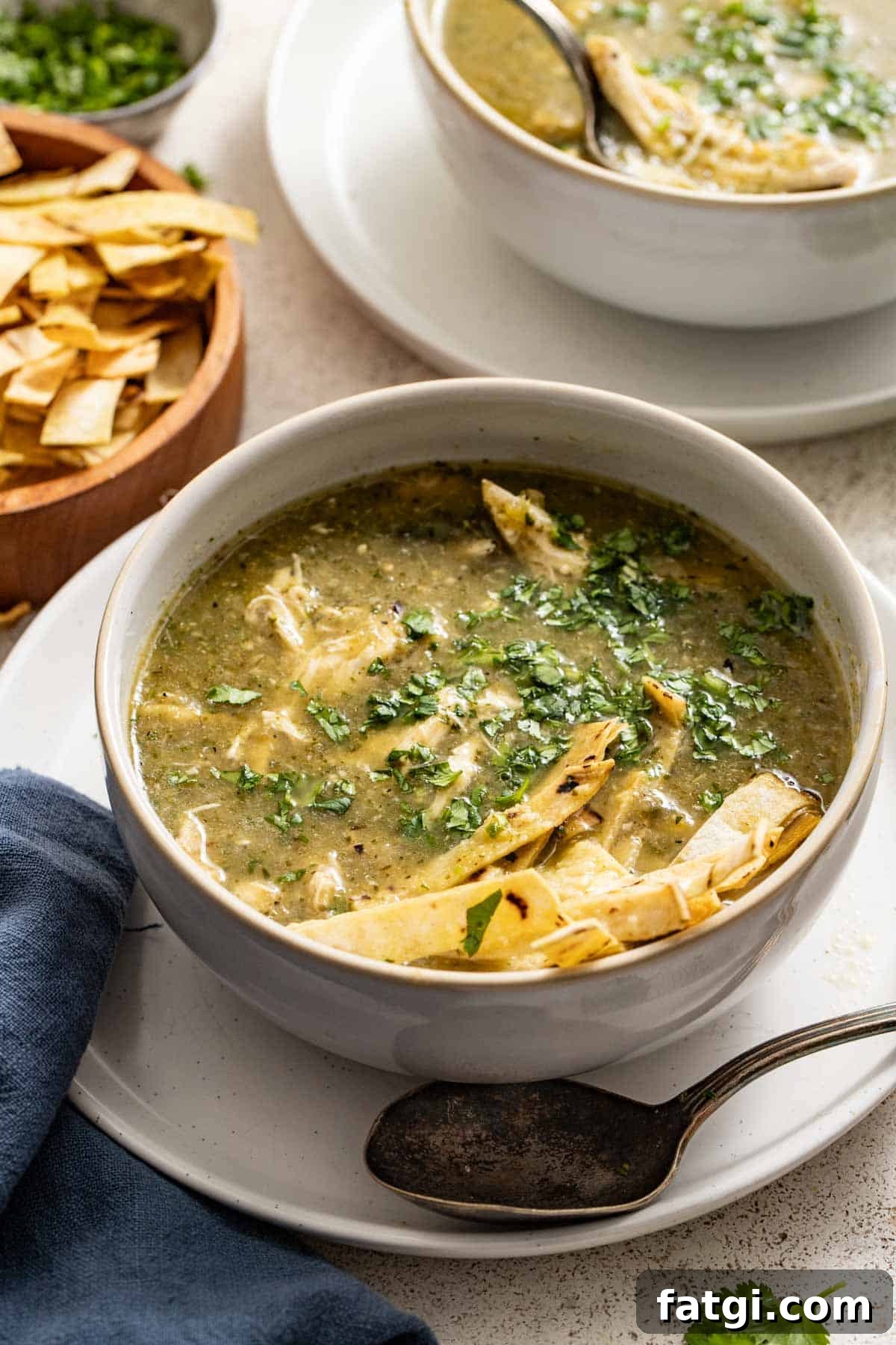 A bowl of chicken enchilada soup topped with tortilla chips, next to a spoon.