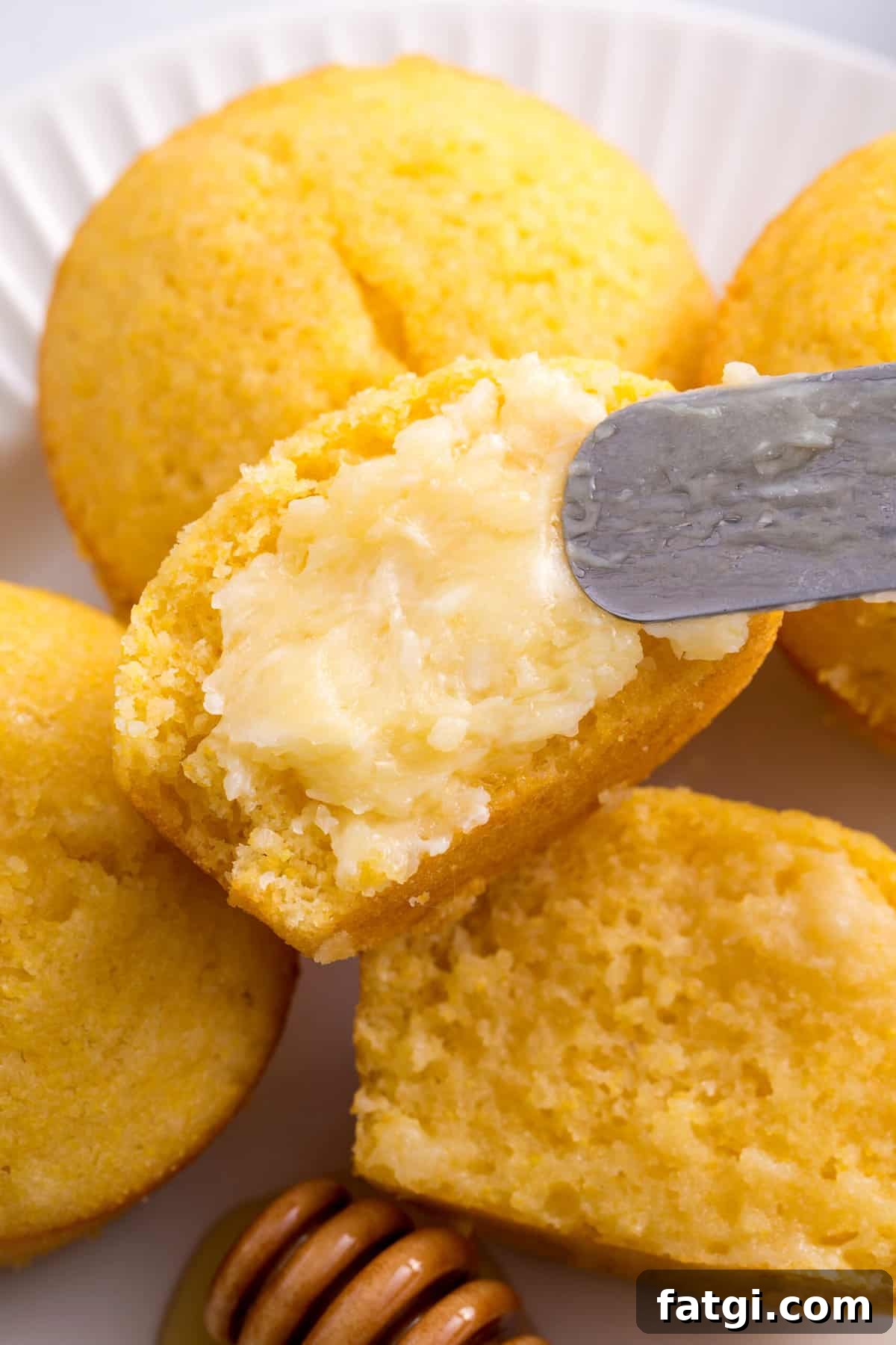 Homemade Corn Muffins with Honey Butter Recipe 2 close up image of corn muffin halves spread with homemade honey butter with a metal spatula.