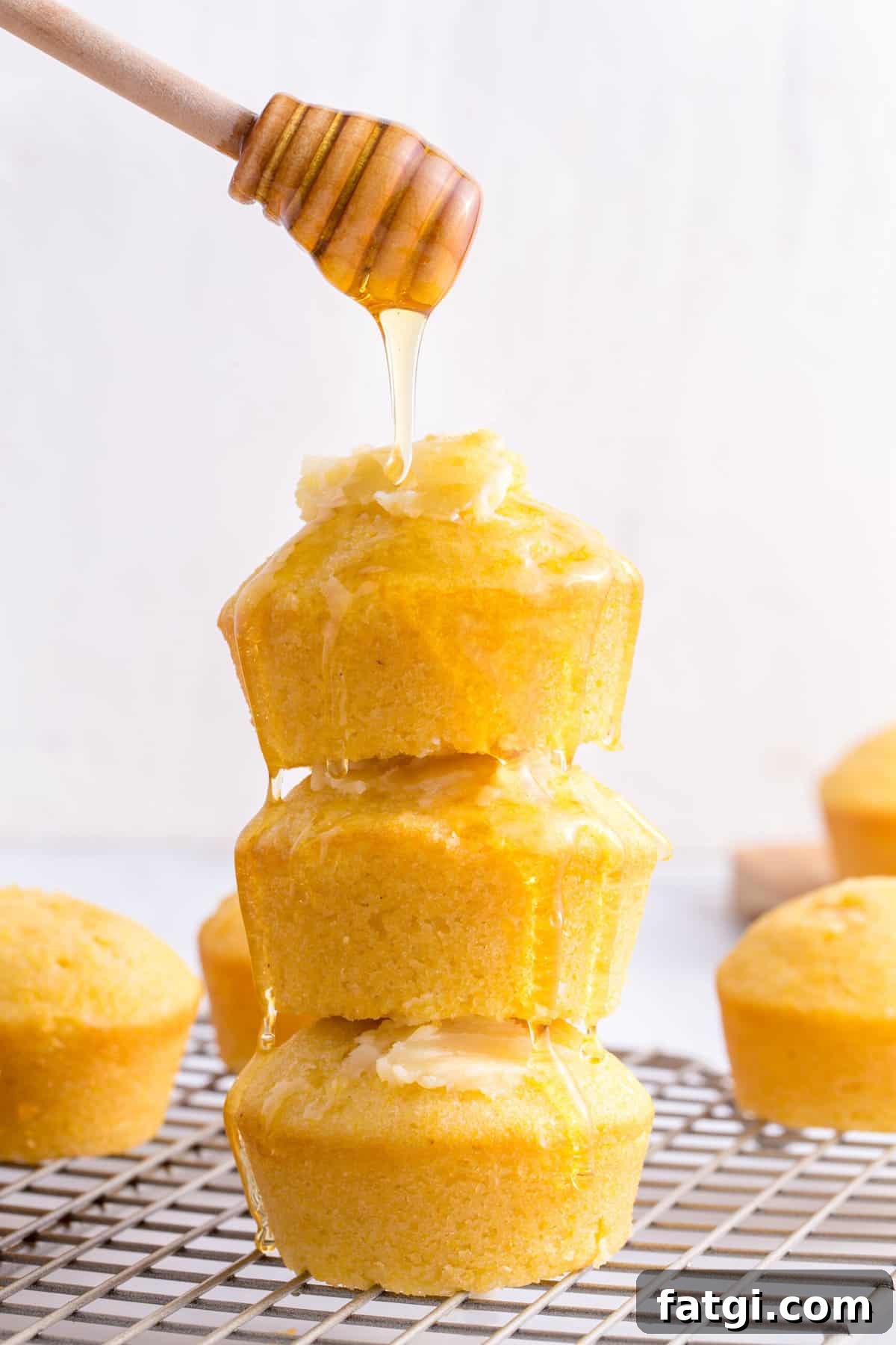 Homemade Corn Muffins with Honey Butter Recipe 3 honey drizzled over a stack of three homemade corn muffins topped with honey butter.