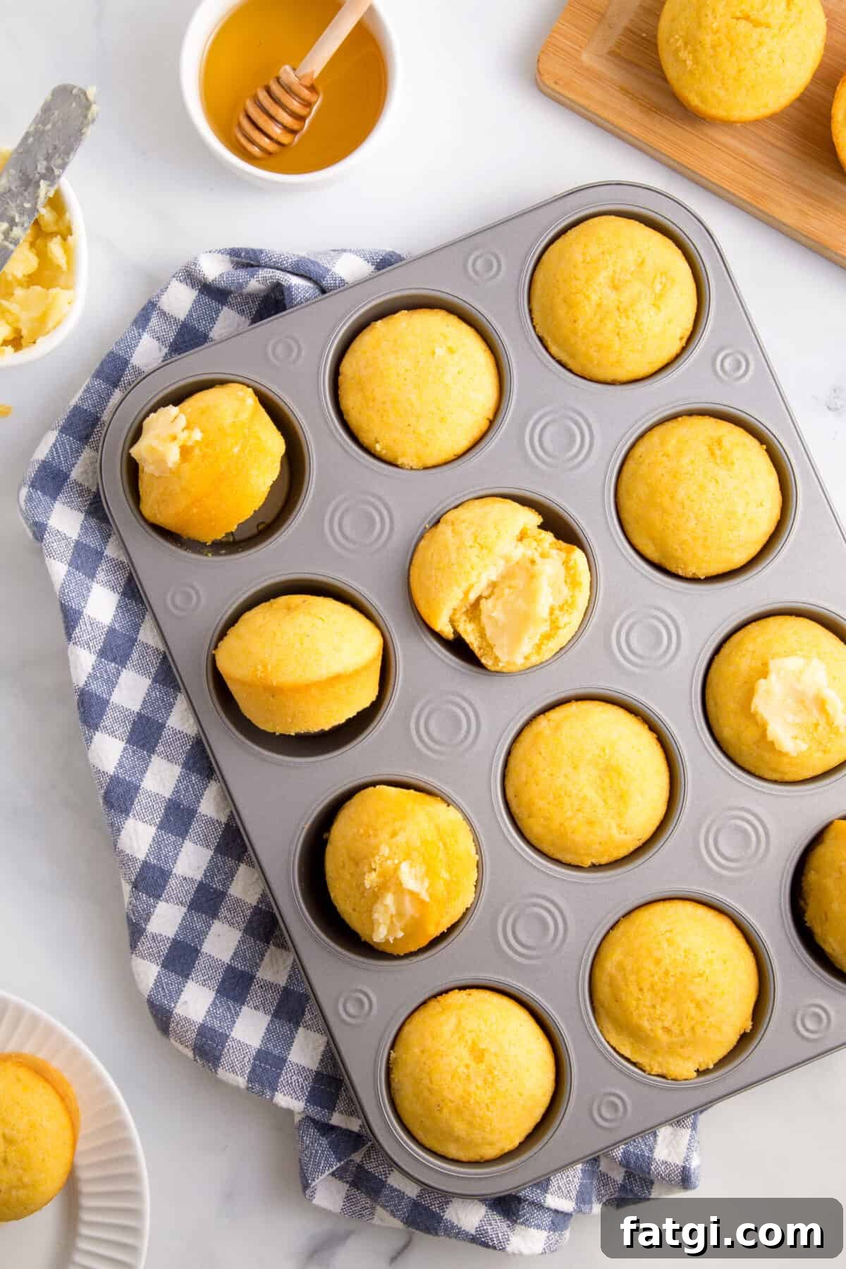 Homemade Corn Muffins with Honey Butter Recipe 4 Overhead image of a pan of corn muffins with a few topped with butter.