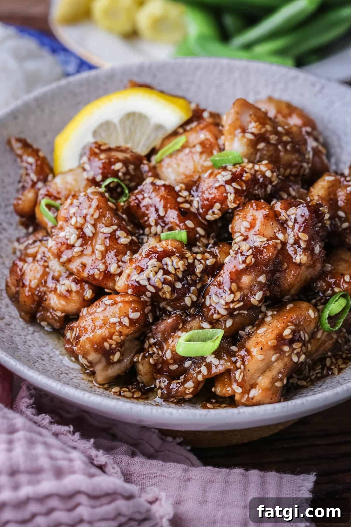 Sticky Lemon Chicken in a bowl with a slice of lemon and scattered with spring onions.