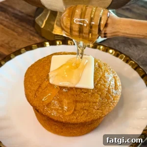 Sweet Potato Honey Cornbread Recipe 9 Honey being drizzled over a sweet potato honey cornbread muffin topped with a pat of butter on a decorative white plate.