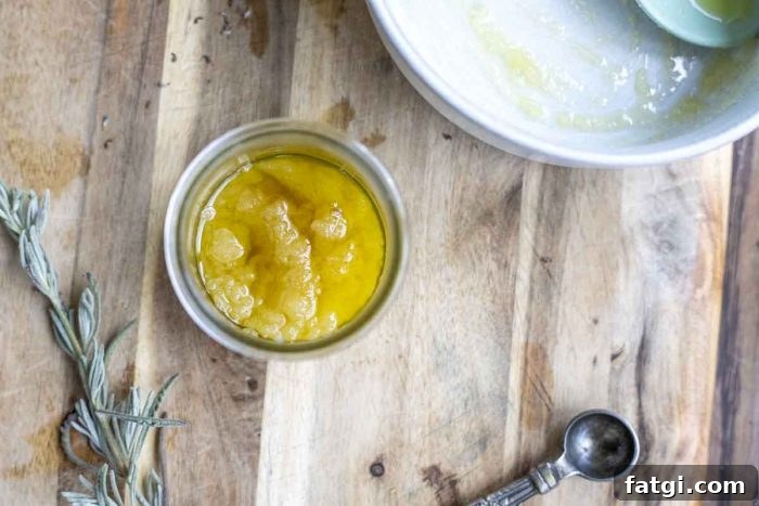 overhead photo of a scalp sugar scrub in a glass jar on a wooden cutting board with a measuring spoon and lavender in the front with a white bowl in the back
