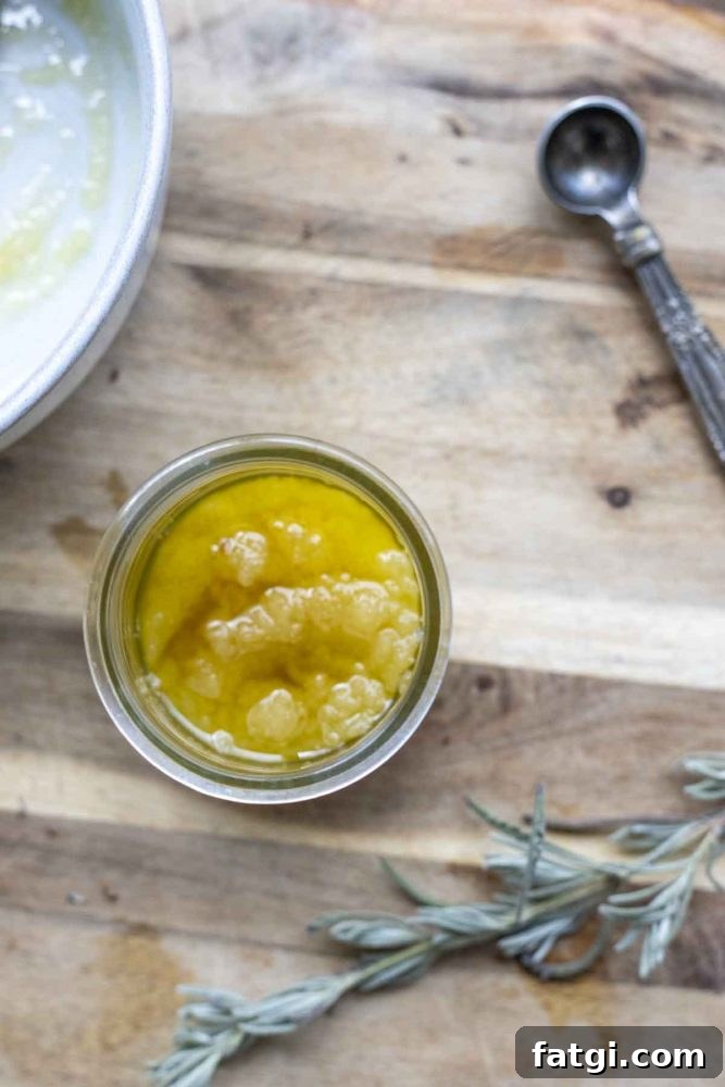 overhead photo of a jar of scalp exfoliating scrub on a wood cutting board with a spring of lavender, a measuring spoon and a bowl around the jar