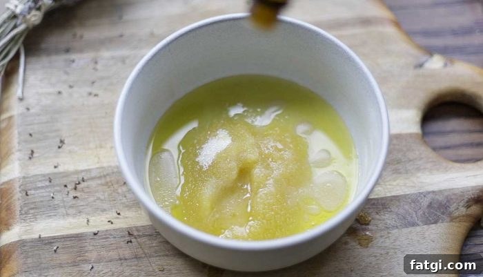 adding essential oils to a scalp scrub in a bowl on a wood cutting board