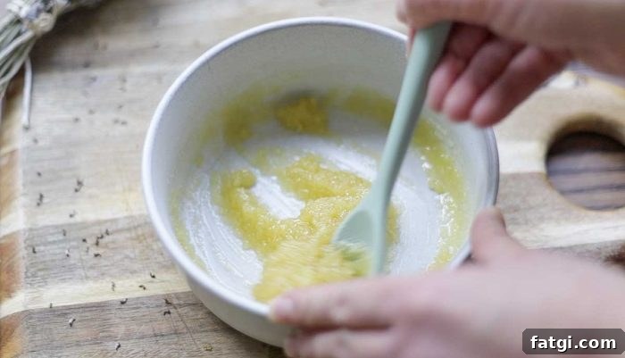 teal silicon spoon mixing together diy scalp scrub in a cream bowl on a wooden cutting board