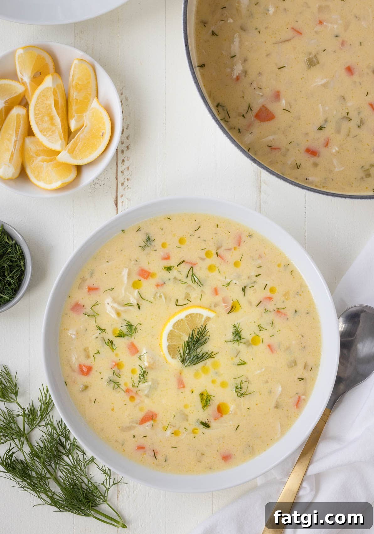 Greek lemon chicken soup, called avgolemono, in a white bowl with lemon slice and fresh dill.