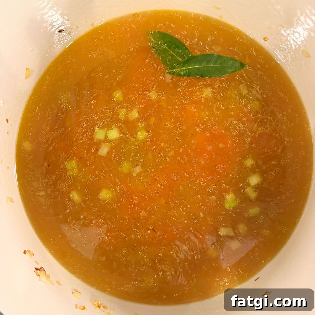 A pot of golden chicken broth with cooked vegetables for a soup base.