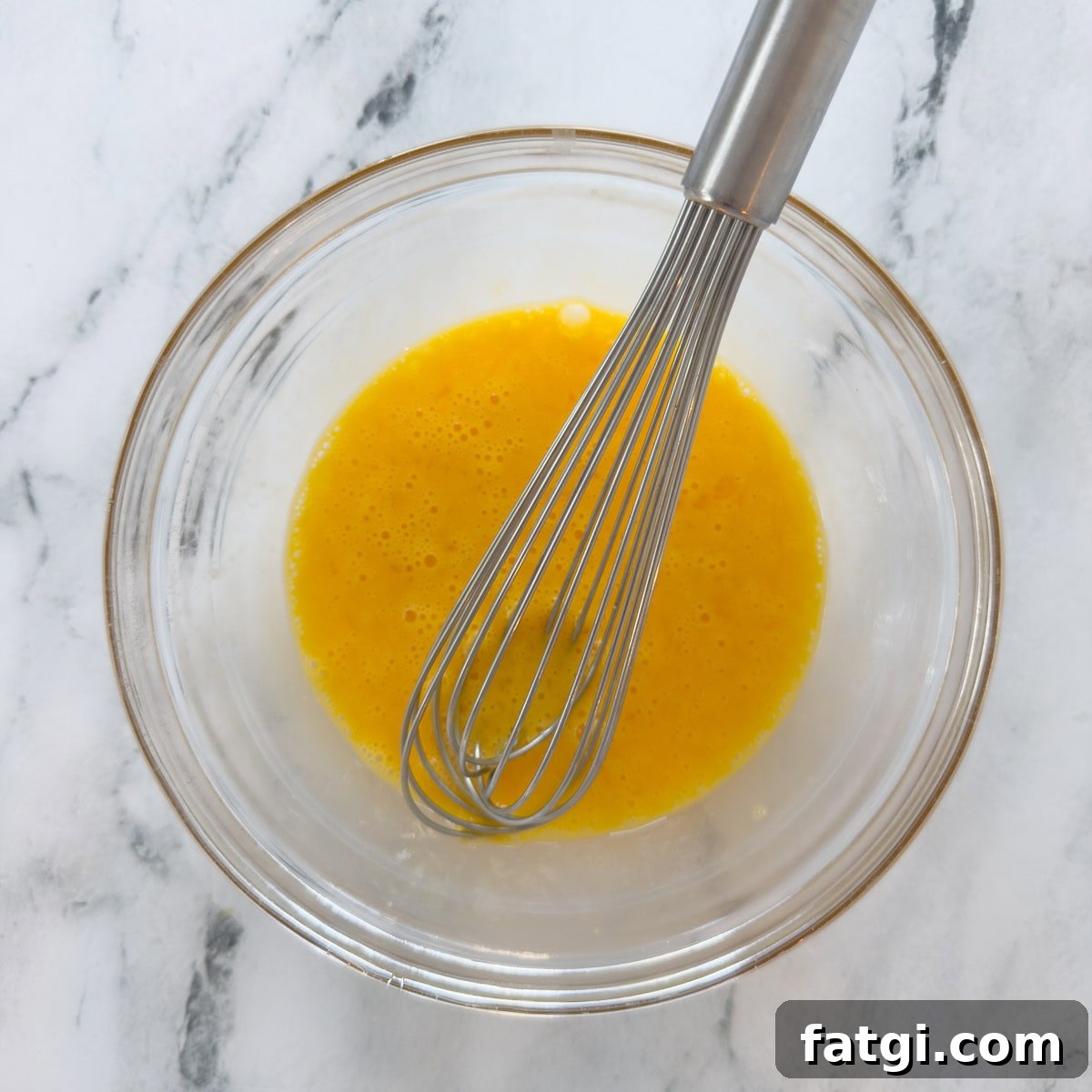Whisking eggs and lemon juice together in a glass bowl.