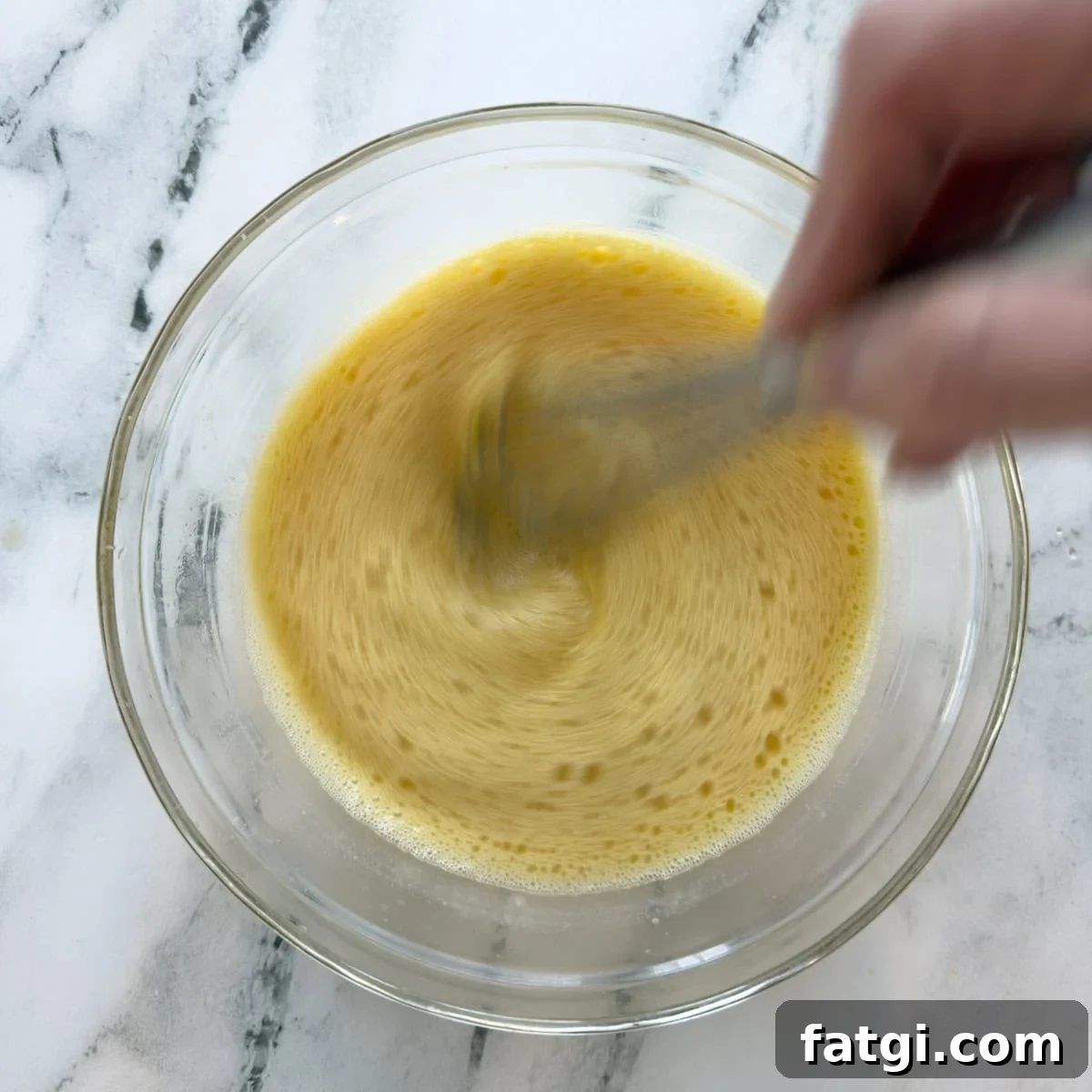 Tempering eggs, broth and lemon juice together with a silver whisk.