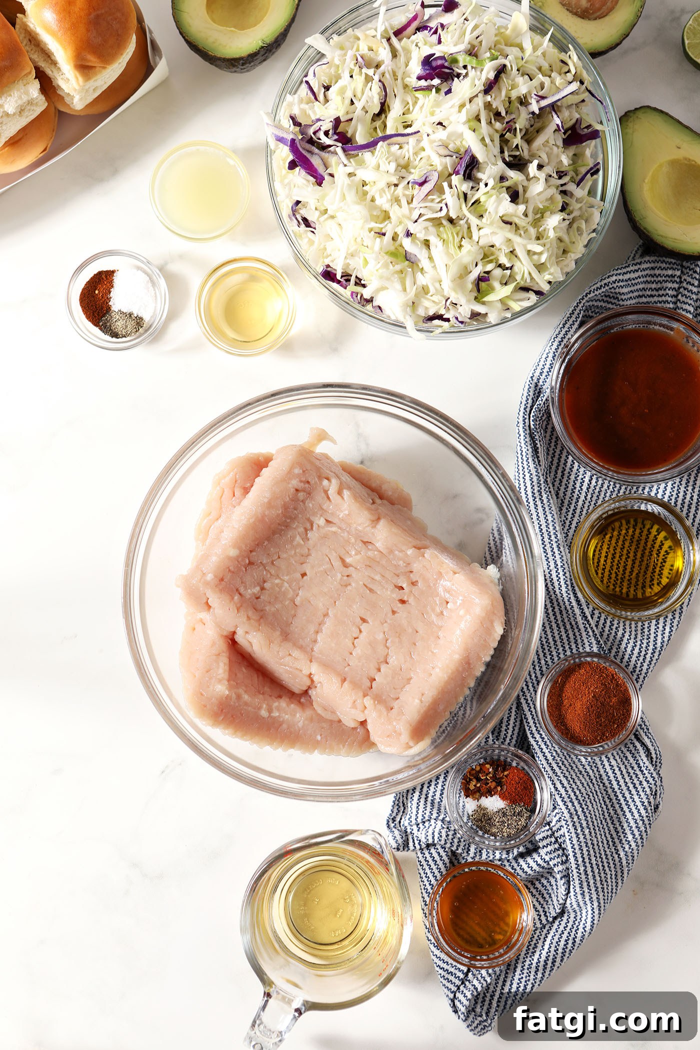 Ingredients to make bbq chicken sliders and avocado coleslaw in bowls on a white surface