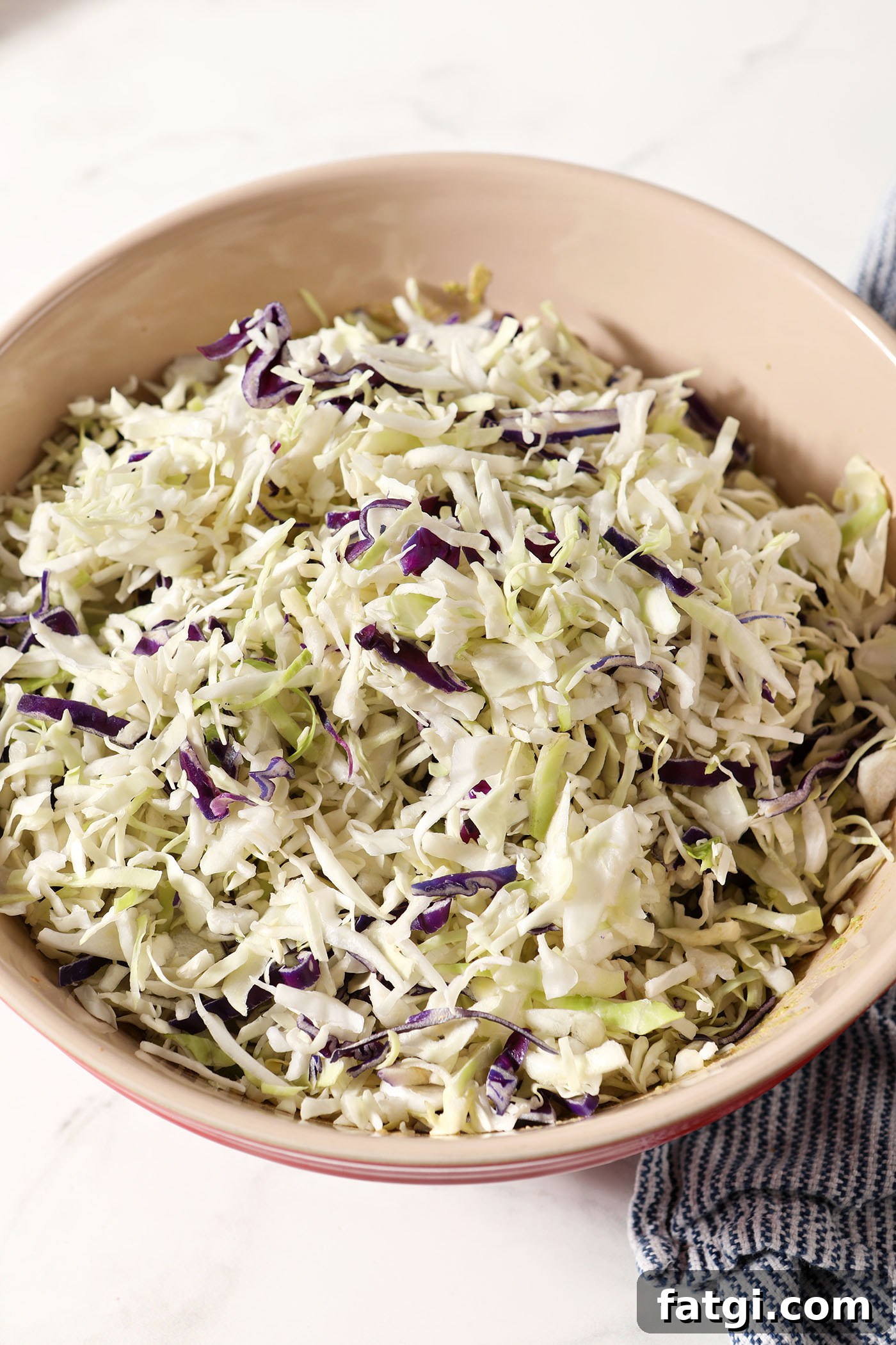Shredded cabbage sits on top of smashed avocados in a bowl on a white surface