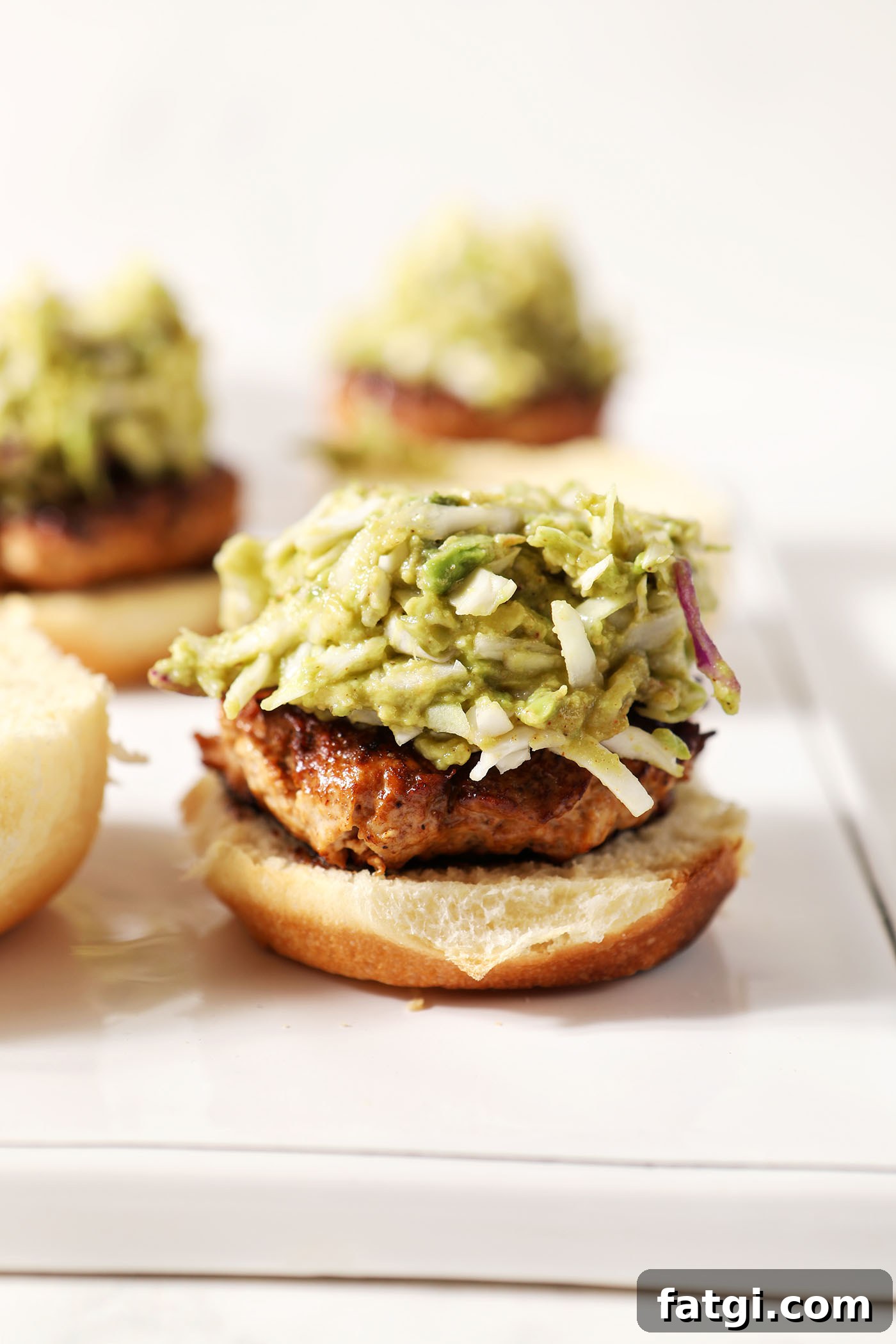 Avocado coleslaw on top of a bbq chicken burger on a white platter