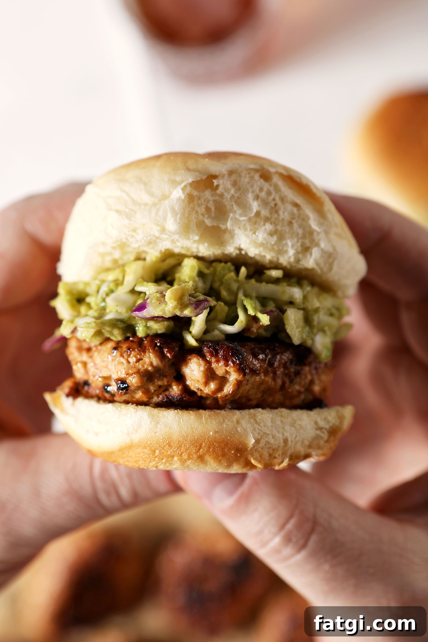 Hands hold a BBQ Chicken Slider with Avocado Slaw above a marble surface
