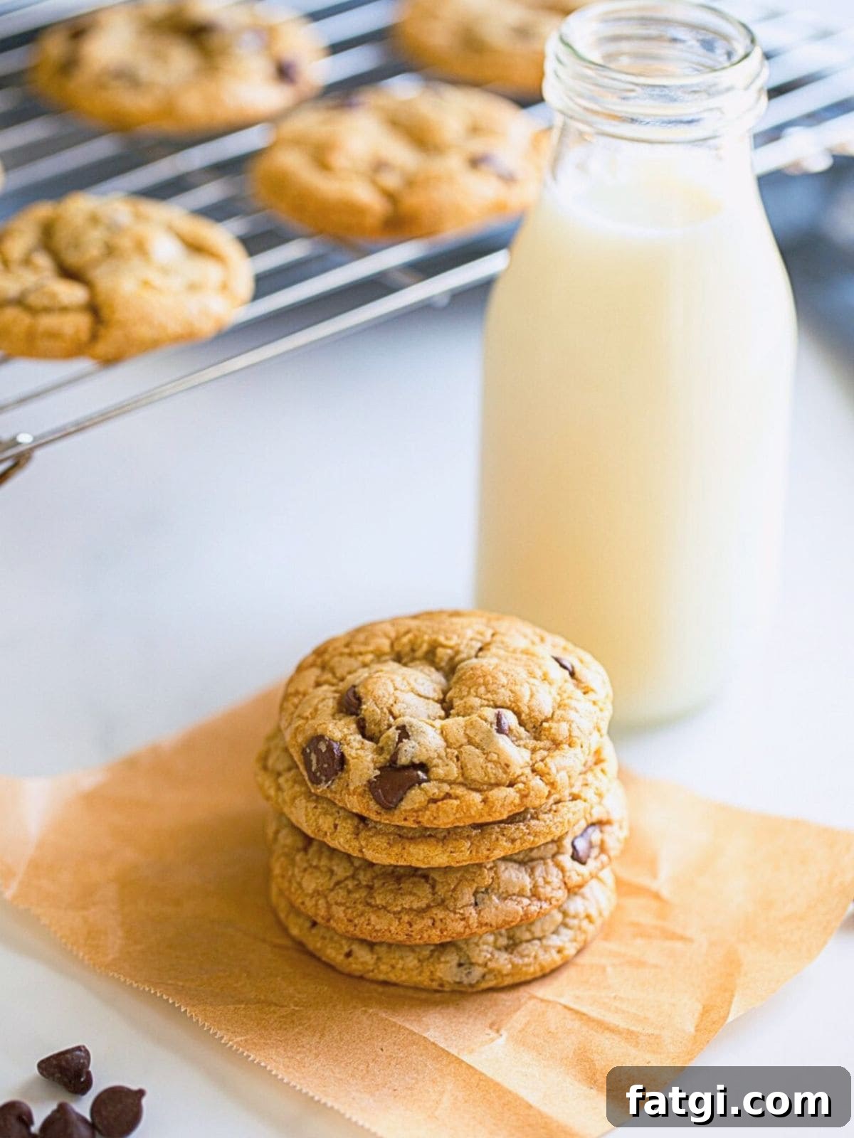 Stack of three no chill chocolate chip cookies on parchment paper after being baked with cooling cookies in background.