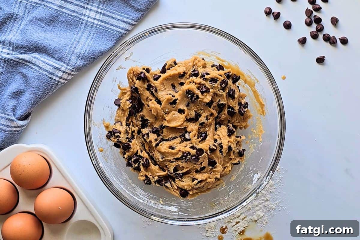 Homemade chocolate chip cookie dough in glass mixing bowl loaded with chocolate chips.