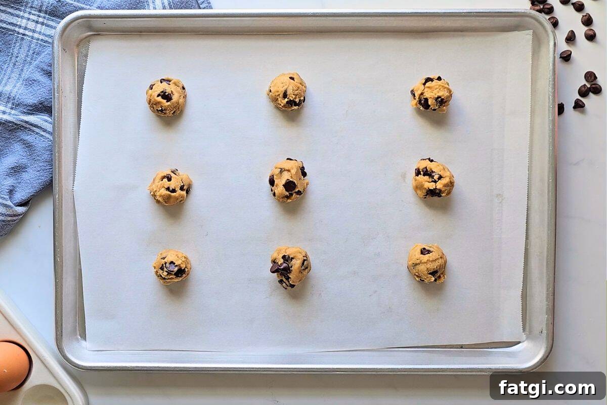 Chocolate Chip cookie dough balls evenly spaced out on baking sheet lined with parchment paper.