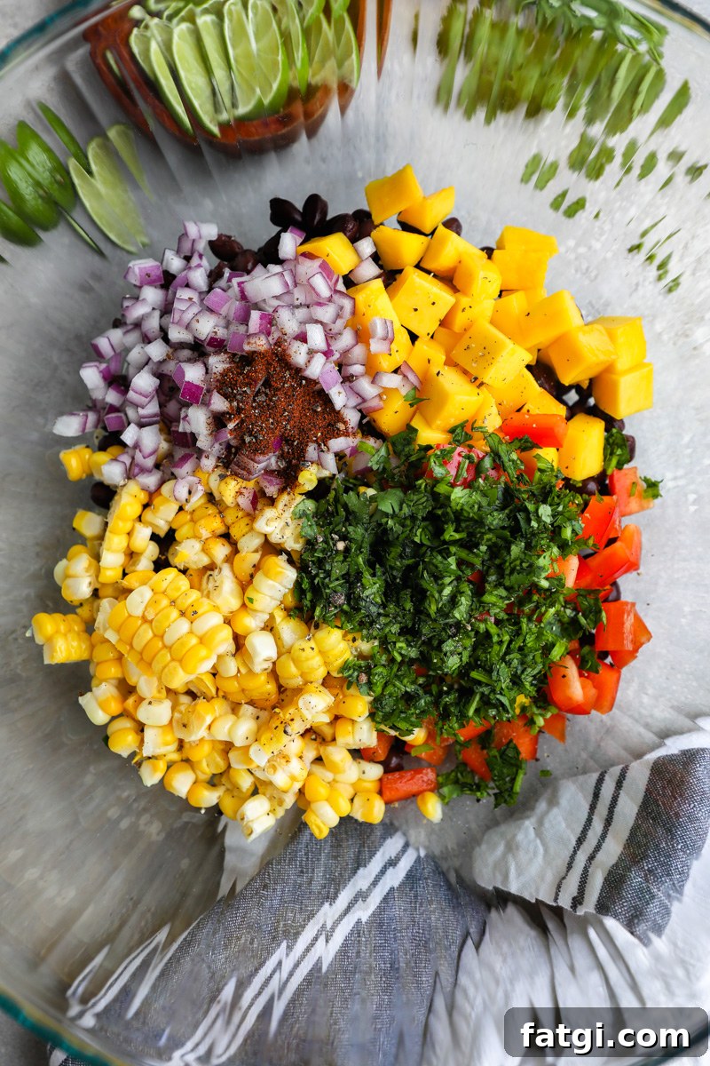 Zesty Black Bean, Mango and Avocado Salad 4 A large clear bowl filled with black beans, mango, bell pepper, fresh corn red onions, cilantro and spices sitting next to a small bowl of lime wedges