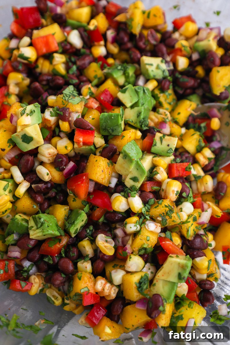 Zesty Black Bean, Mango and Avocado Salad 5 A clear bowl filled wth black bean mango and corn salad with diced avocado on top