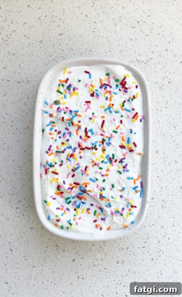 birthday cake baked oats in white ceramic ramekin with greek yogurt icing and rainbow sprinkles on top