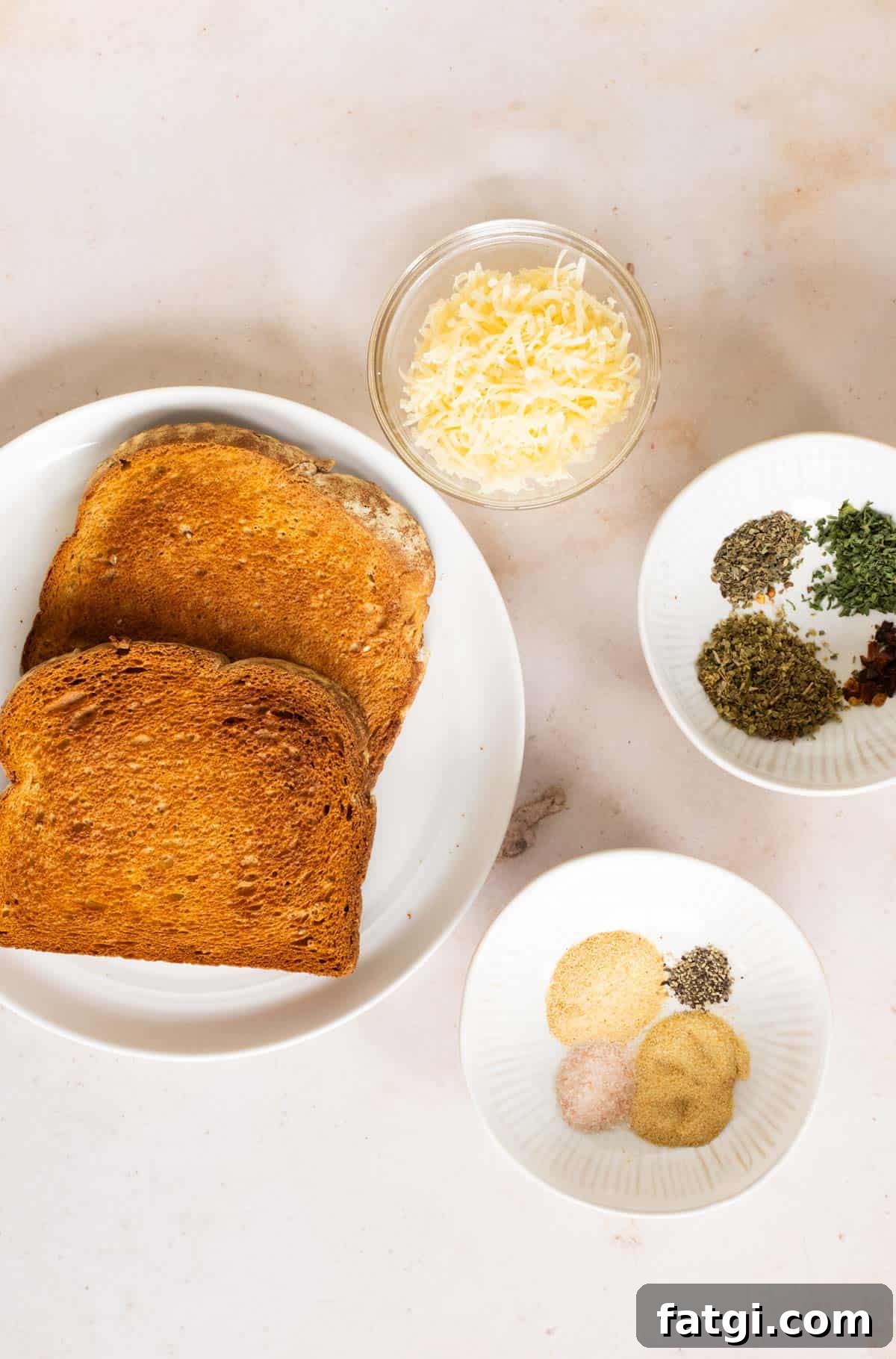 Toasted bread slice, shredded parmesan cheese, Italian spices on white plates.