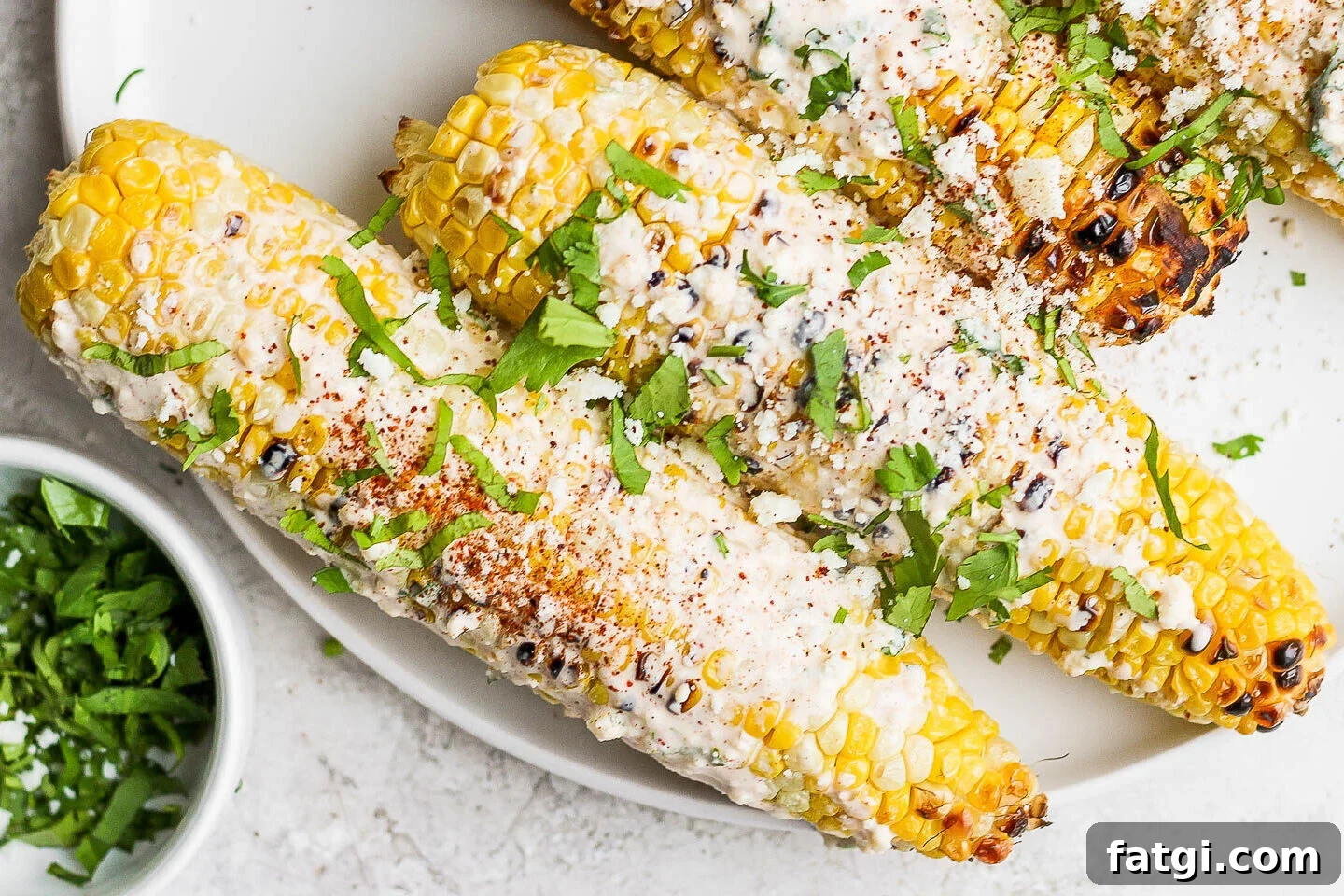 mexican street corn on the cobb on a white plate topped with cilantro and cotija