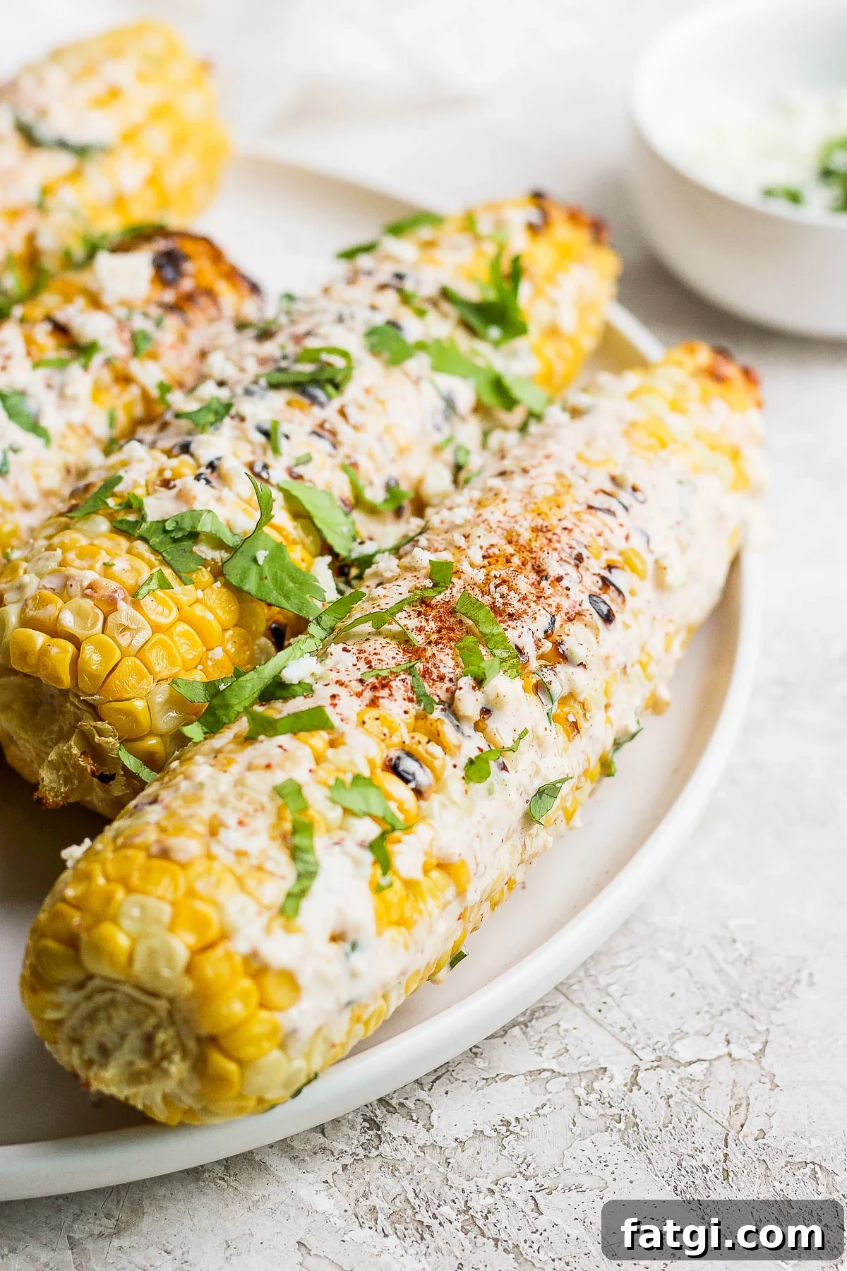 mexican street corn on the cobb on a white plate topped with cilantro and cotija
