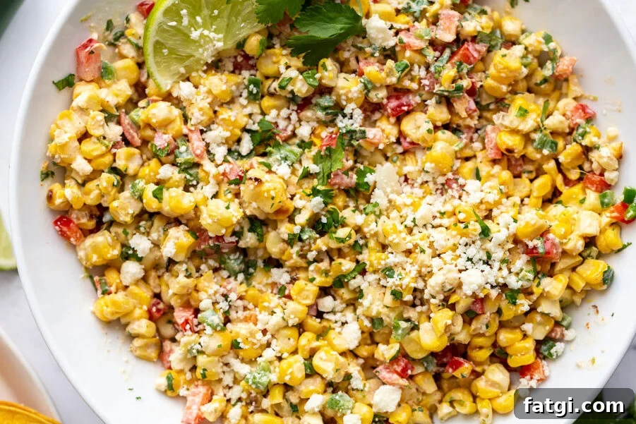 large white bowl of mexican street corn salad topped with cotija cheese and a lime with cilantro in the scene