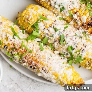 mexican street corn on the cobb on a white plate topped with cilantro and cotija