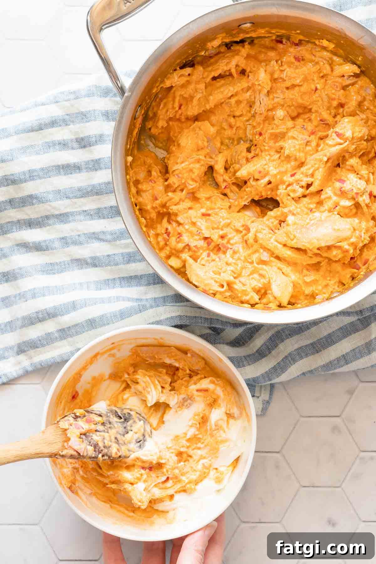 small bowl of yogurt being mixed with some buffalo chicken dip with saucepan of dip on the side.