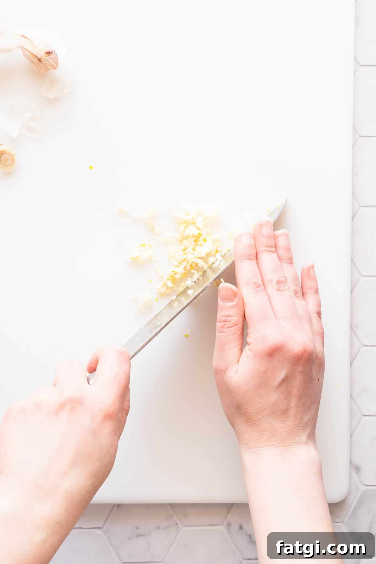 garlic being finely chopped on cutting board.